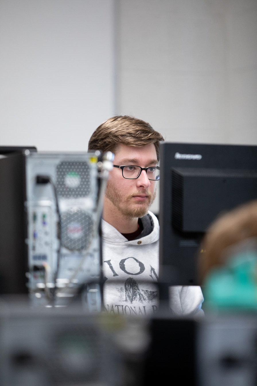 [View framed by a monitor and computer tower of
                        student working on a program]